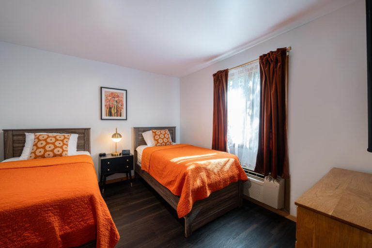 Two beds in a room with orange bedspreads.