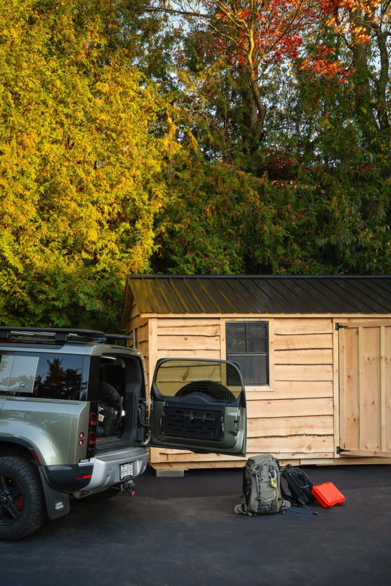A suv is parked next to a wooden shed.