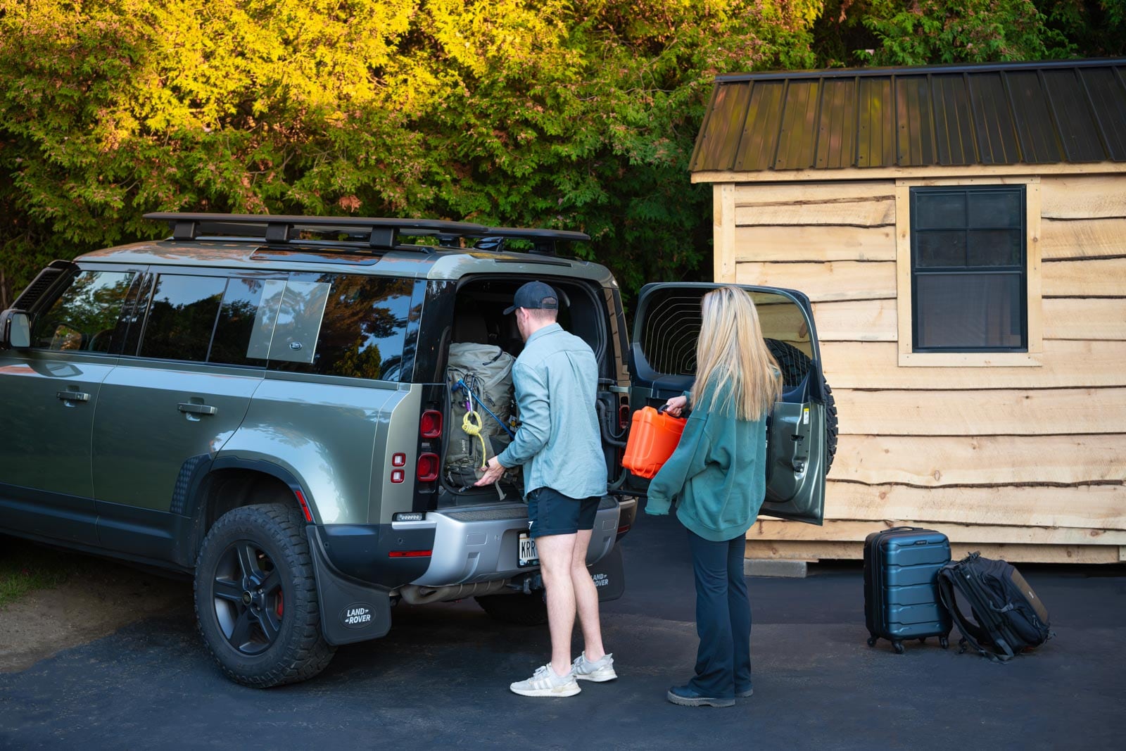 A man and woman are opening the trunk of a land rover.