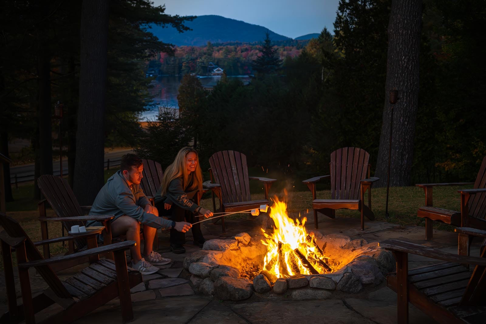Two people sitting around a fire pit at dusk.