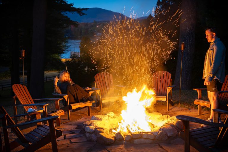 Two people sitting around a fire pit at dusk.