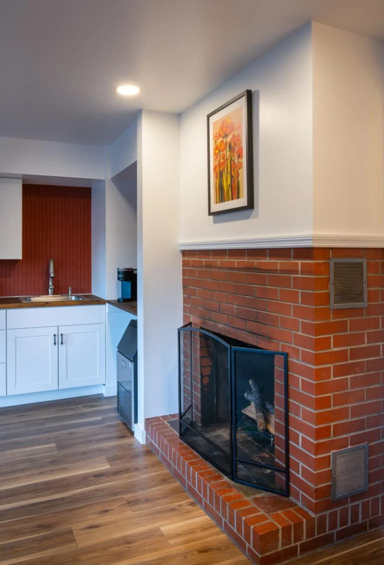 A kitchen with a brick fireplace and white cabinets.