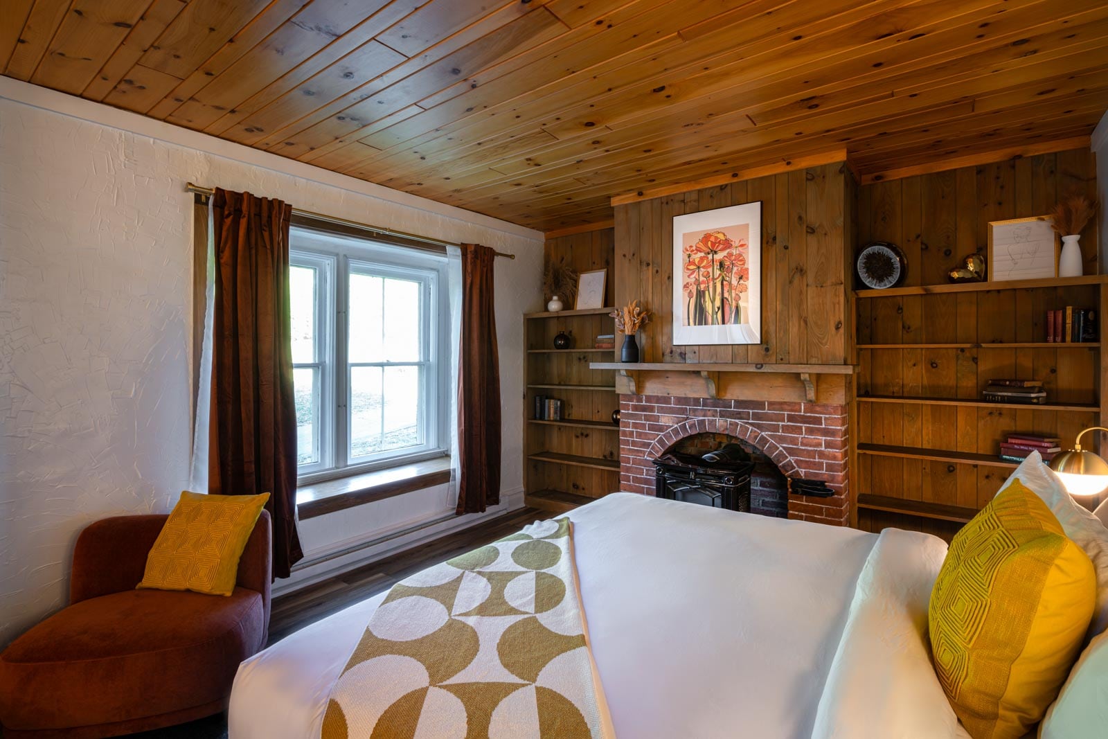 A bed in a room with wood paneling and a fireplace.