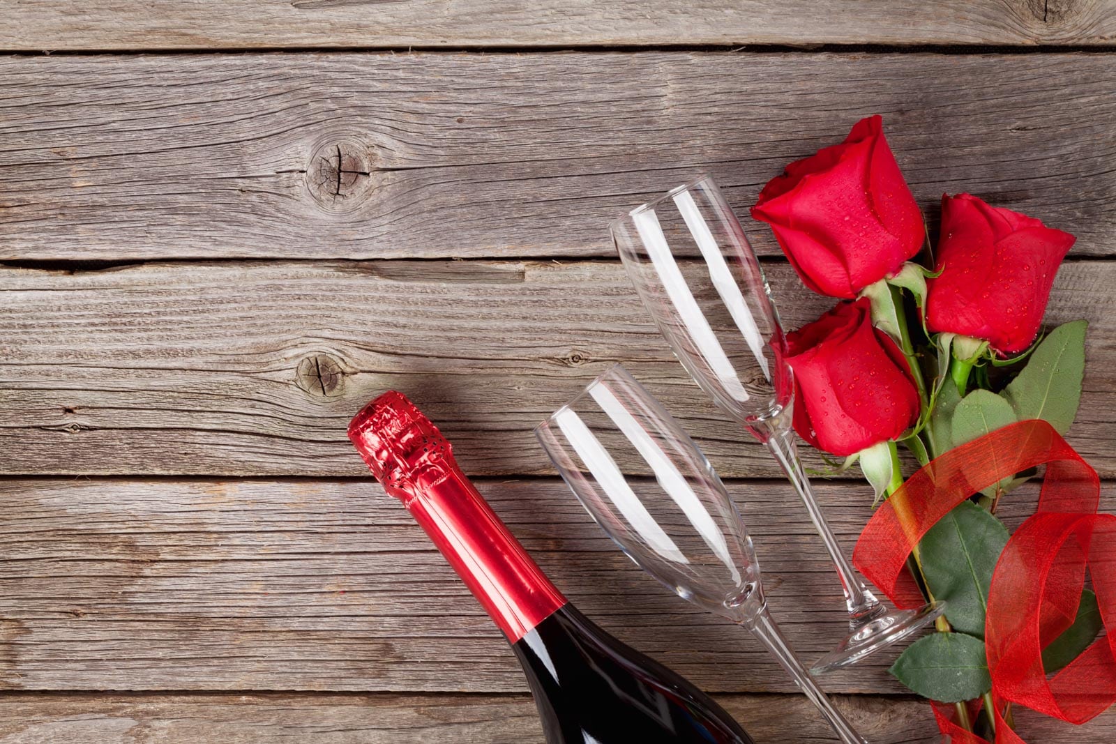 Red roses and a bottle of champagne on a wooden table.