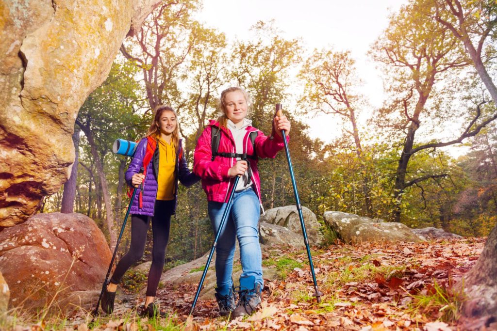 Two girls hiking in the woods with hiking poles.