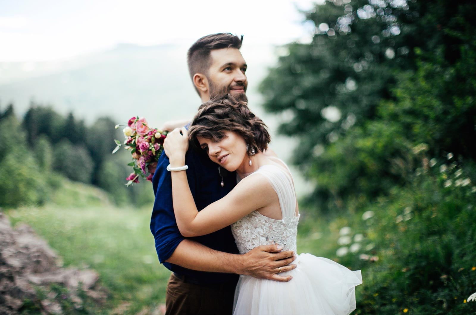 A bride and groom hugging in the mountains.