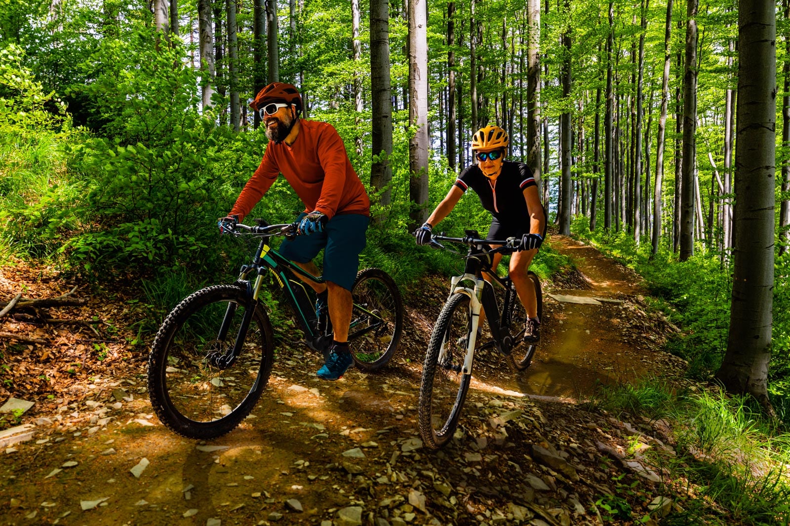 Two mountain bikers riding down a trail in the woods.
