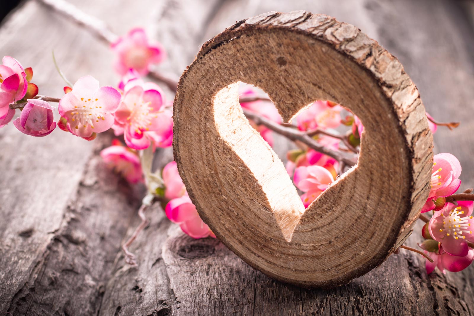 A heart shaped piece of wood with pink flowers.